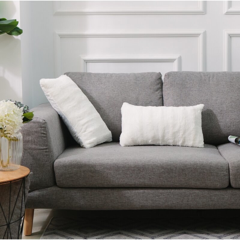 two white faux fur lumbar pillows on a grey couch