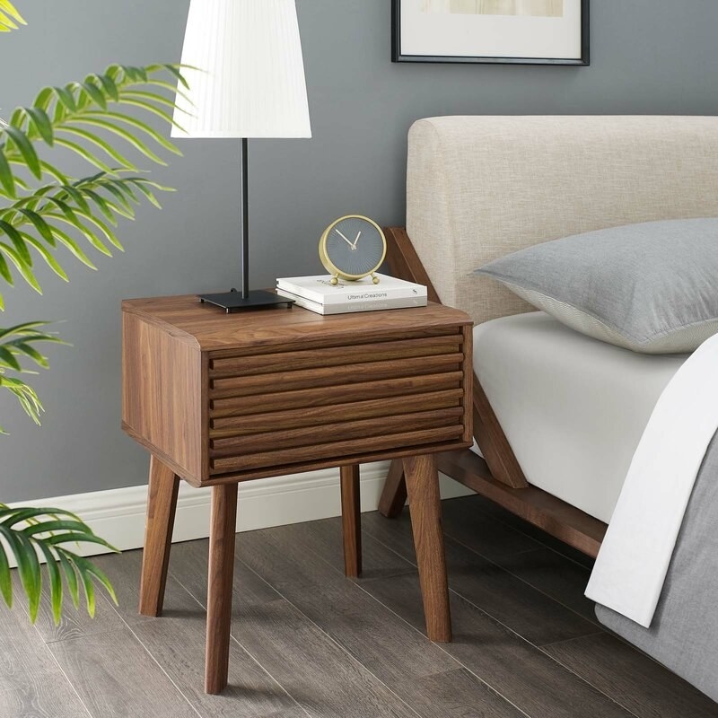 mid-century walnut night stand with drawer next to a bed