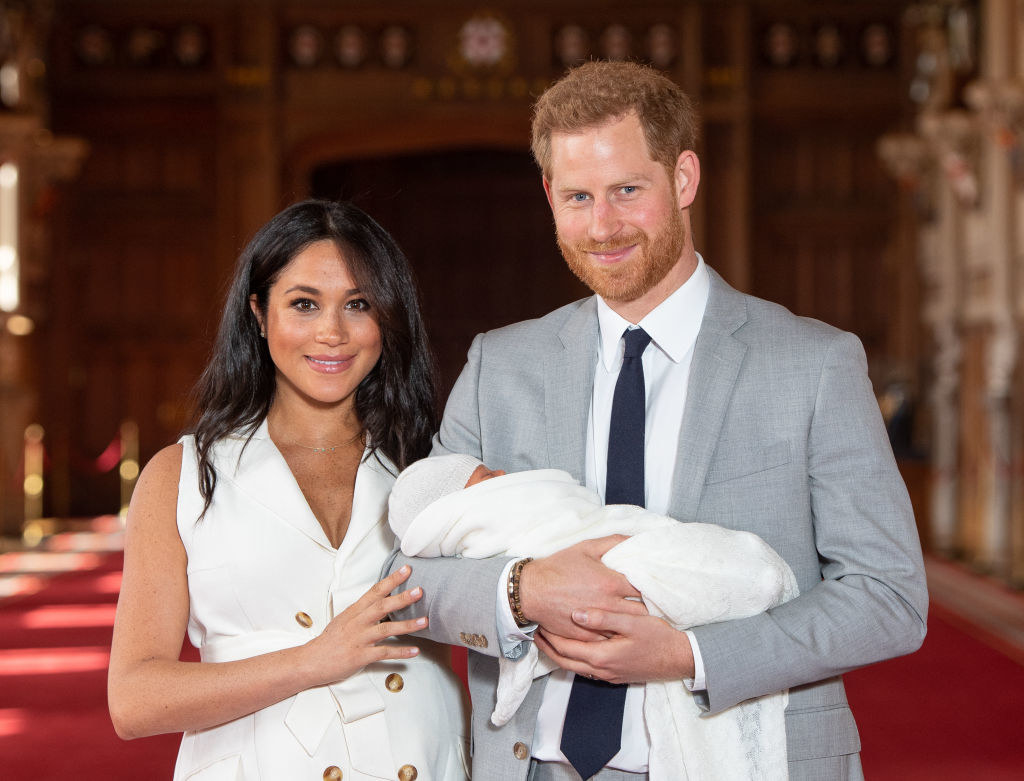 Prince Harry holds then-newborn son Archie Harrison while standing next to Meghan Markle