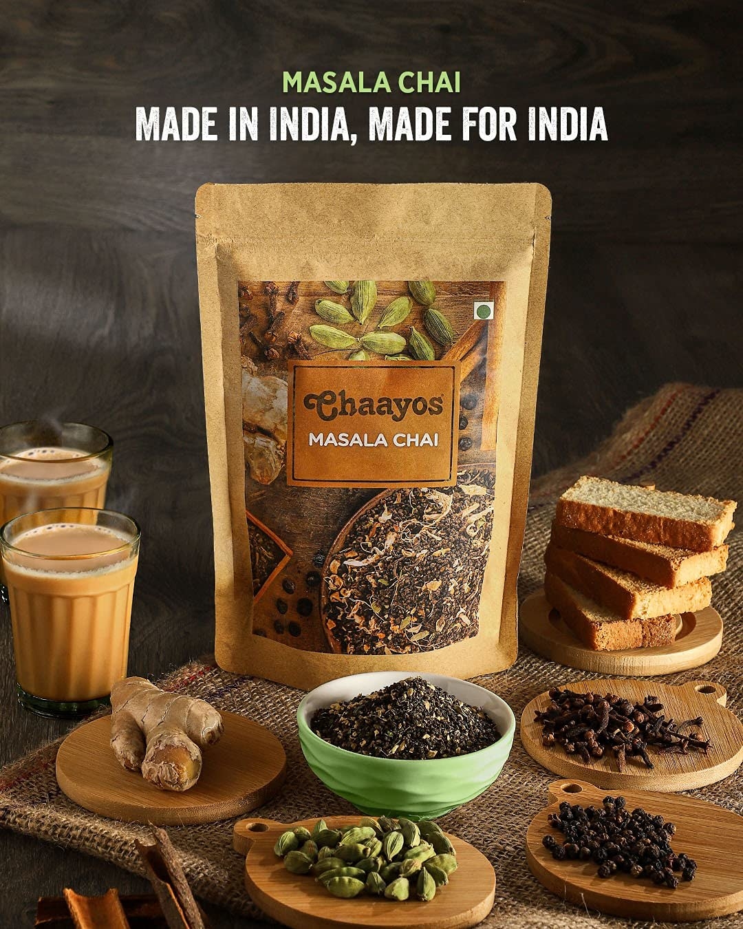 A pack of Masala chai surrounded by whole spices, a stack of rusk and cups of chai.