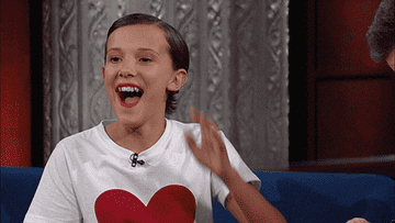 Millie Bobby Brown laughs and covers her face with her hand