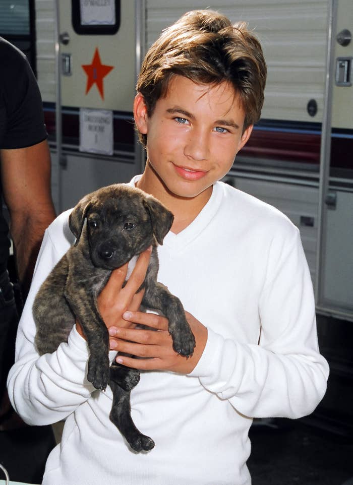 Jonathan Taylor Thomas smiles and holds a puppy in the 1990s