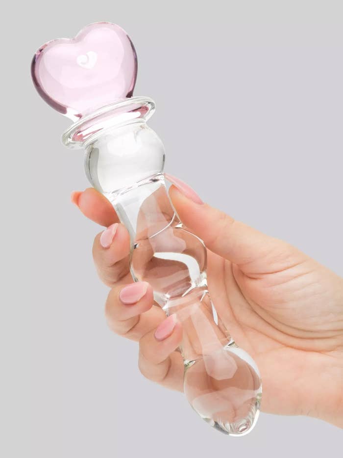 Model holding glass dildo with pink heart-shaped handle