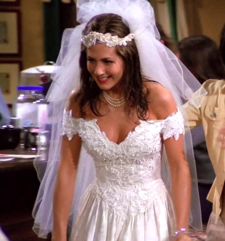 Rachel wearing an off the shoulder dress and an elaborate headpiece