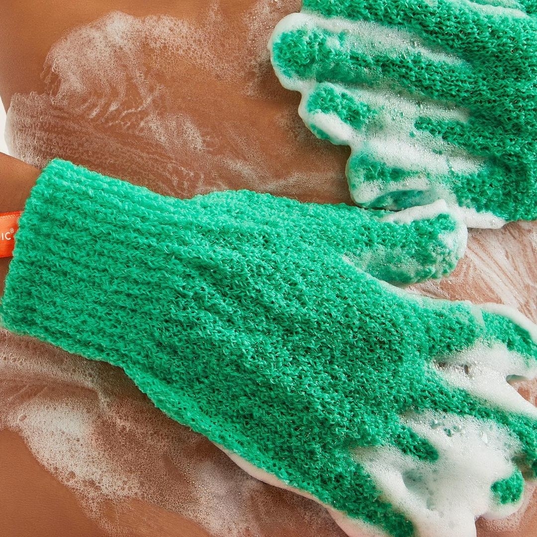 model scrubbing their body with soap using the exfoliating gloves