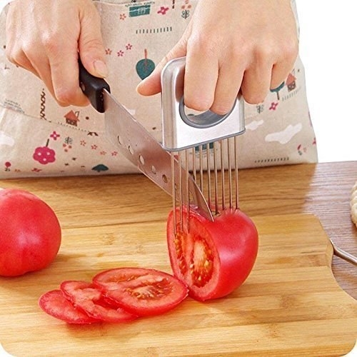 A person using the holder and slicer to hold a tomato in place while slicing it.