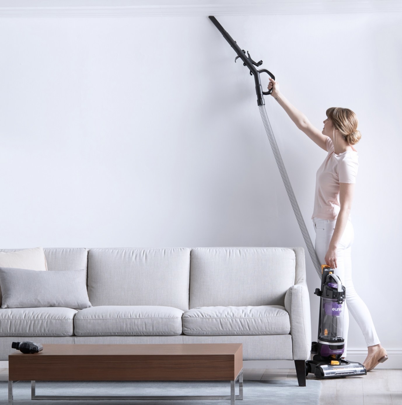An adult vacuums on the ceiling with the hose attachment