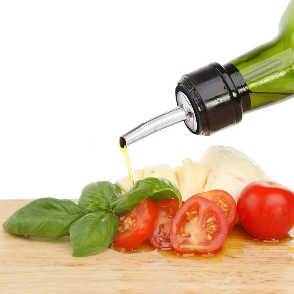 A person pouring oil through the pourer on some cheese, tomatoes and basil.