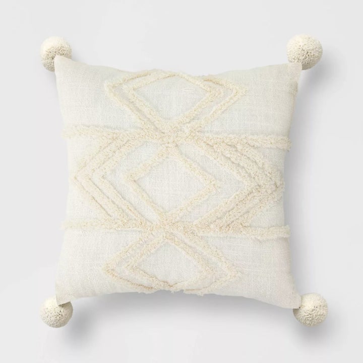 the cream pillow with a geometric design and poms on the corners