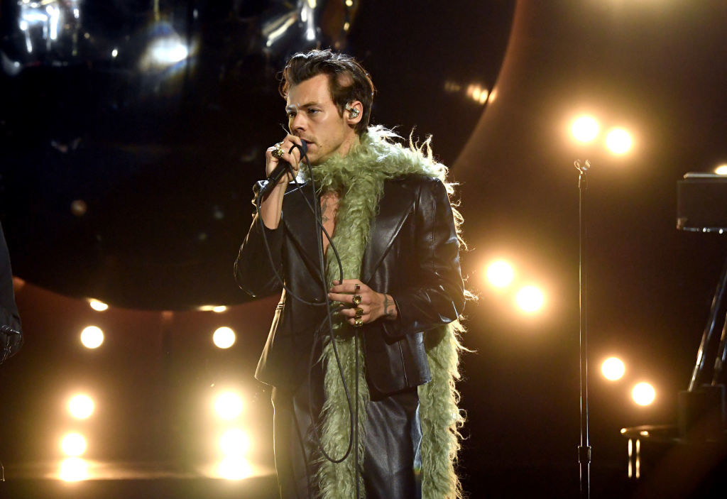 Styles performing on stage in a green boa scarf at the Grammy Awards