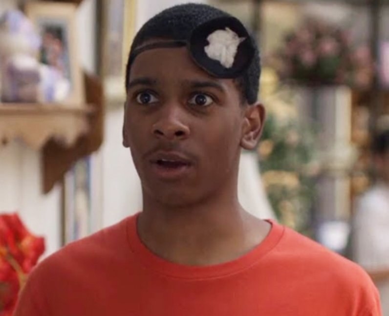 Jamal wears a black and white headband with a flower on it, and an orange t shirt