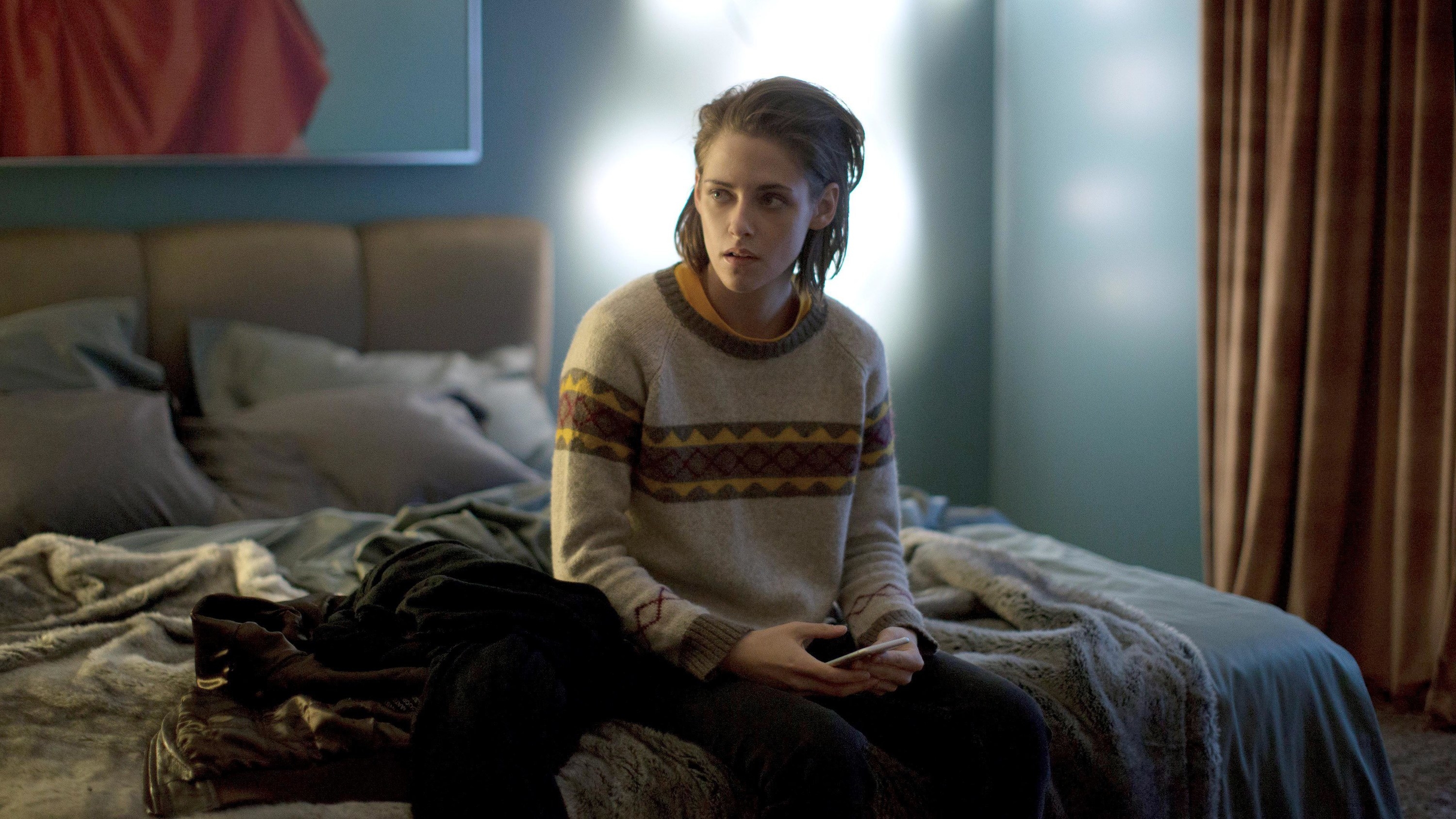 Kristen Stewart sits on a bed looking distressed