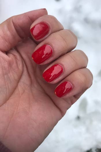 a reviewer with the top coat set to their red-painted nails