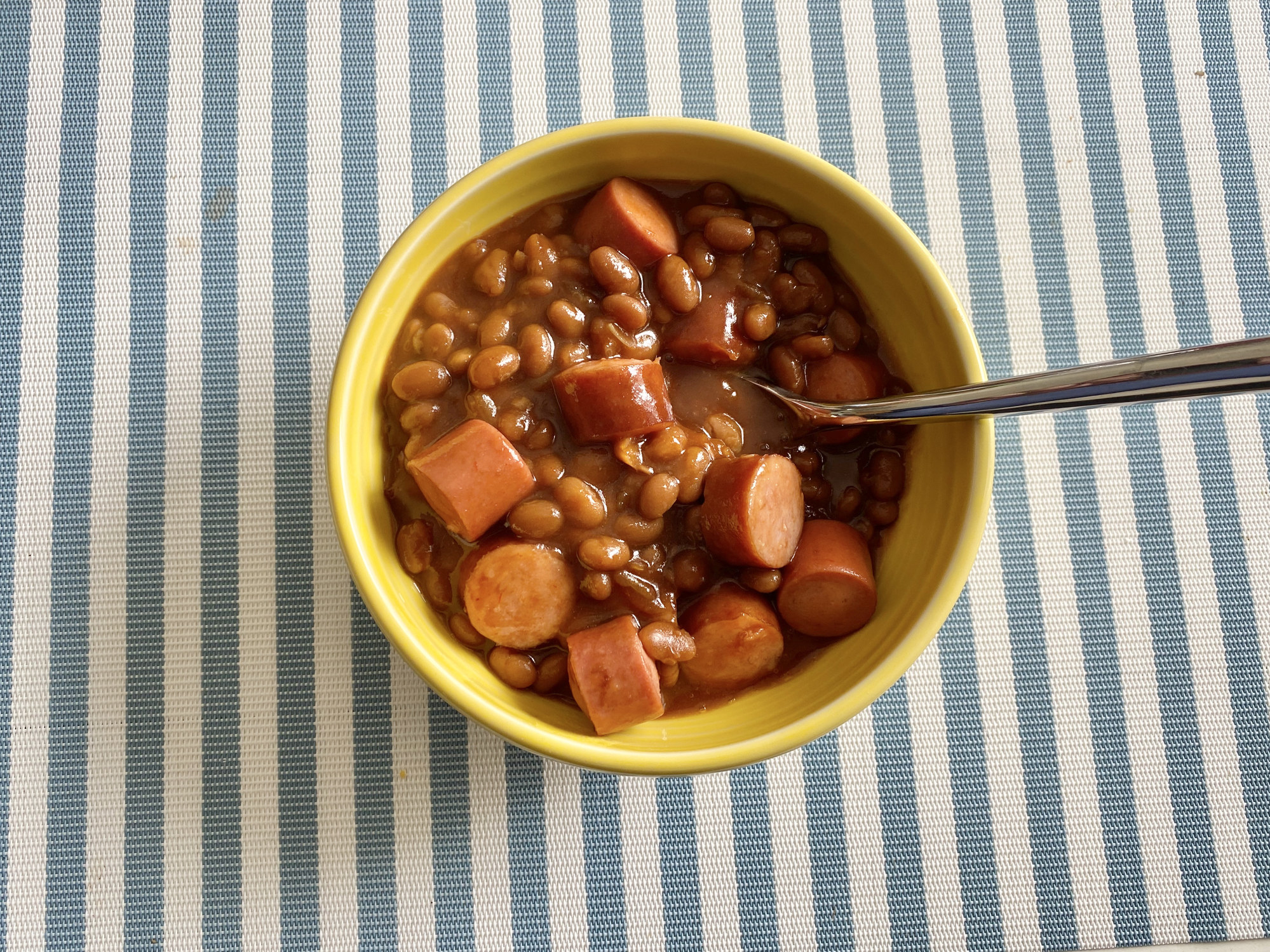 A bowl of baked beans with sliced hot dogs