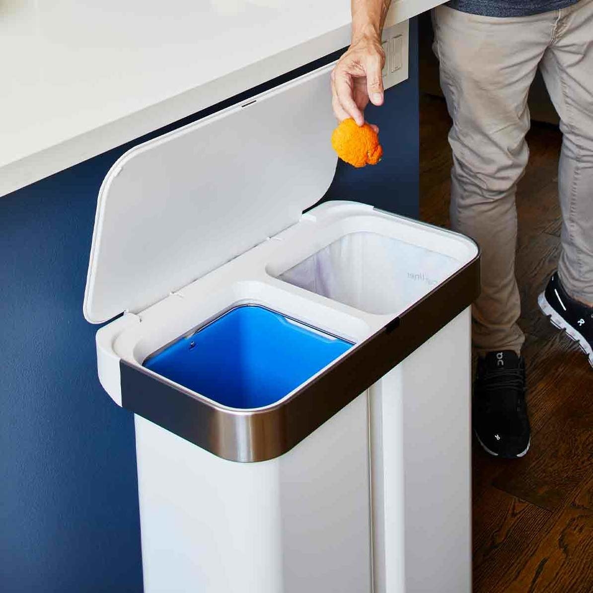 A person throwing an orange peel in the trash can
