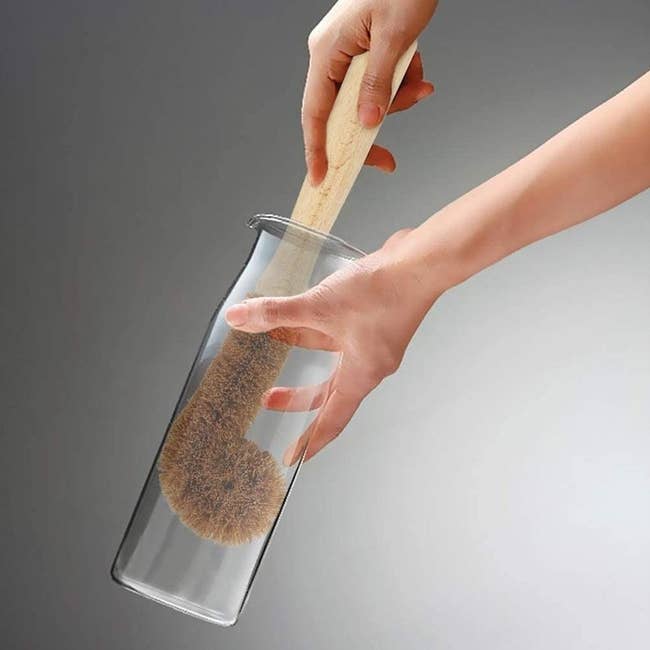Hand pushes brown scrubber down a narrow glass