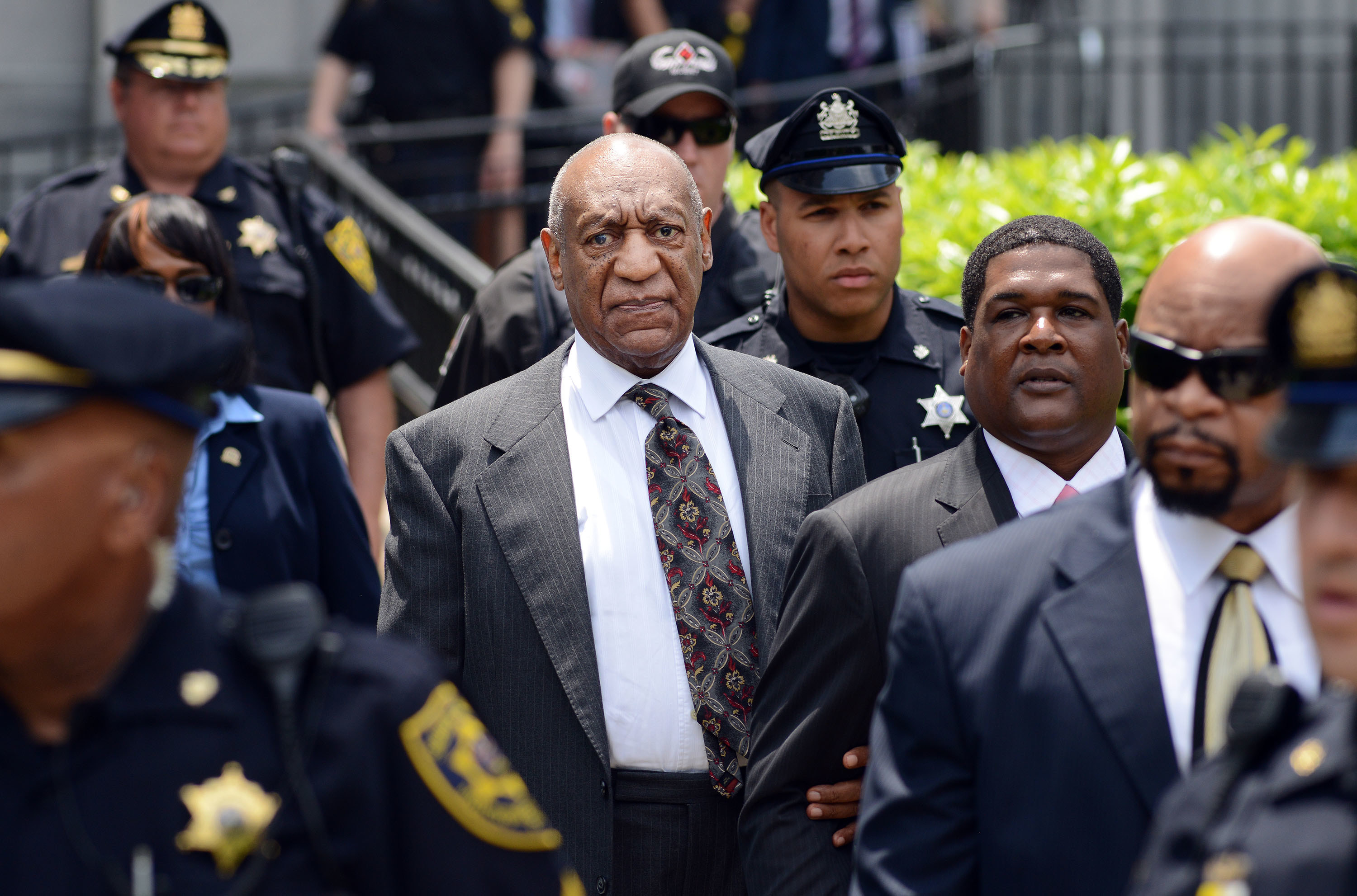 Bill looks serious while heading to a court appearance surrounded by police