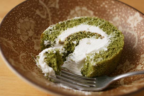 Fork in matcha swiss cake roll with a heavy serving of cream filling.