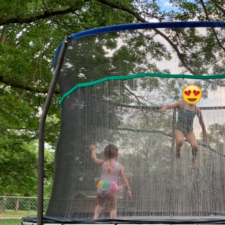 Reviewer's children jumping on the trampoline as the sprinkler hose sprays water on them