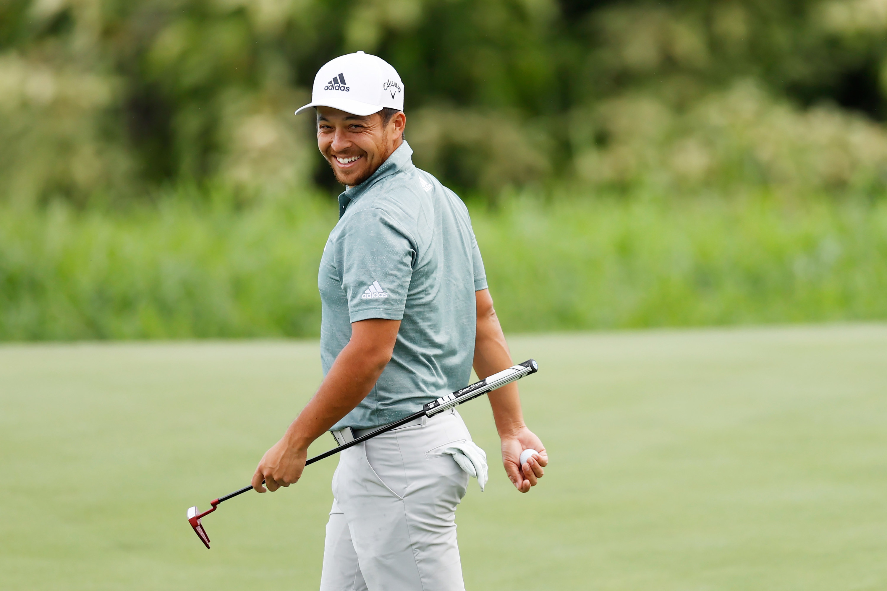 Xander Schauffele smiles while holding his putter