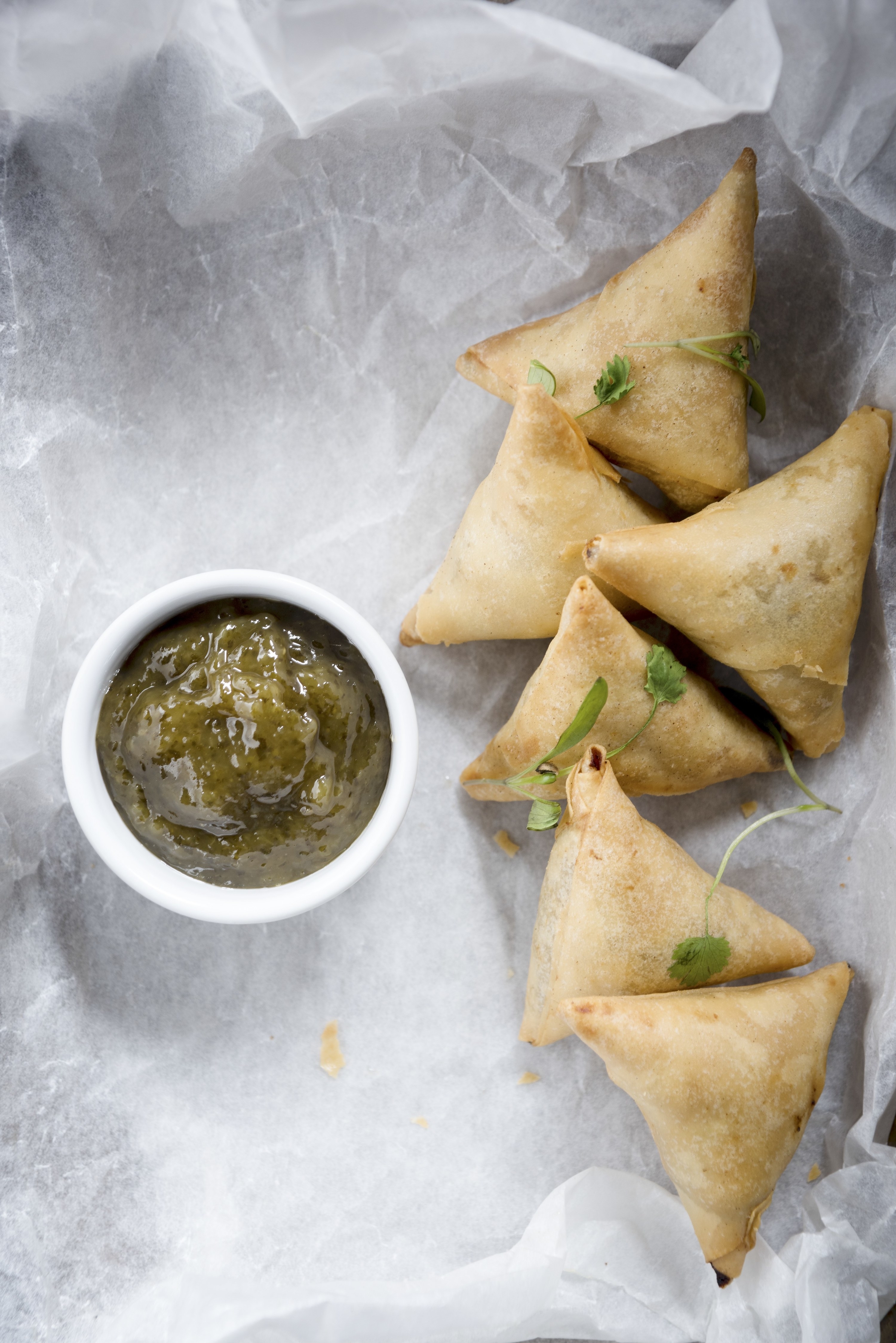 Six samosas with mint and mango chutney are on top of white paper