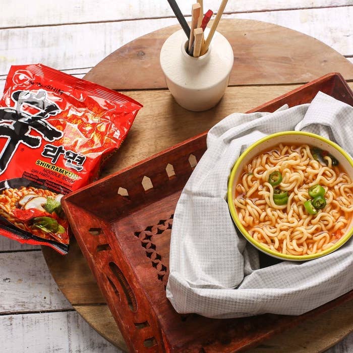 A bowl of soupy ramen with chopsticks and an empty packet of red Nongshim ramyun kept on the side.