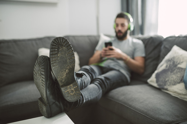 A man sitting on a couch listening to music on his headphones and looking at his phone