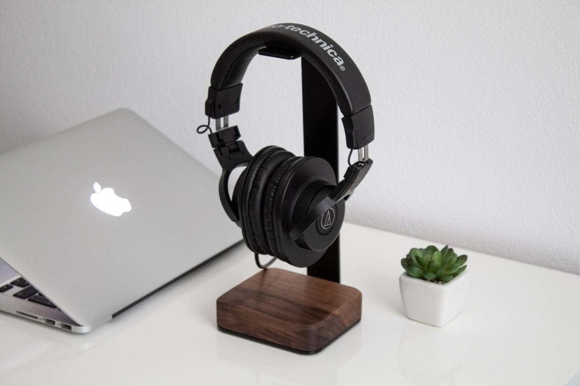A steel and wooden headphone stand with a pair of headphones hung on it