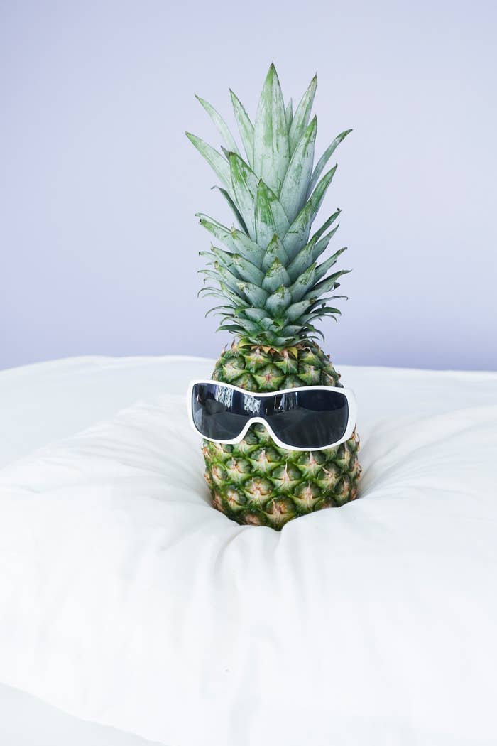 A pineapple is sitting on a white bed wearing white sunglasses
