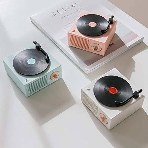 Three different gramophone bluetooth speakers with a rotating vinyl disc on top in the colours white, pastel pink and teal