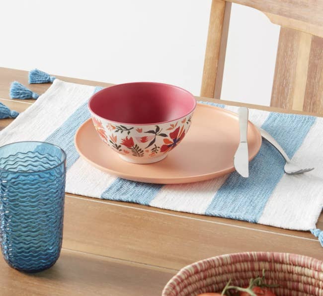 a place setting sitting on top of a blue and white striped placemat with tassles