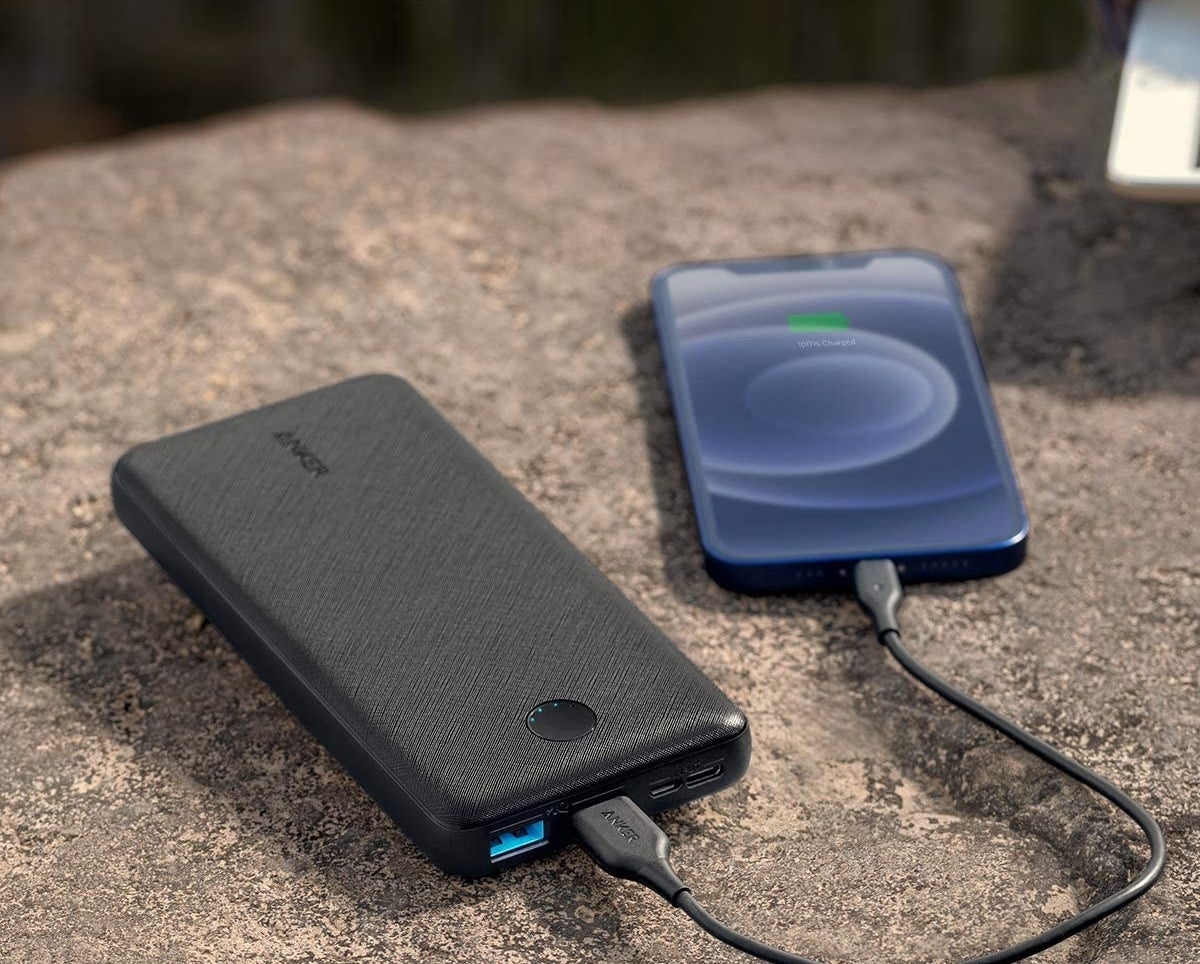 A phone charging using a slim rectangular power bank charger beside it