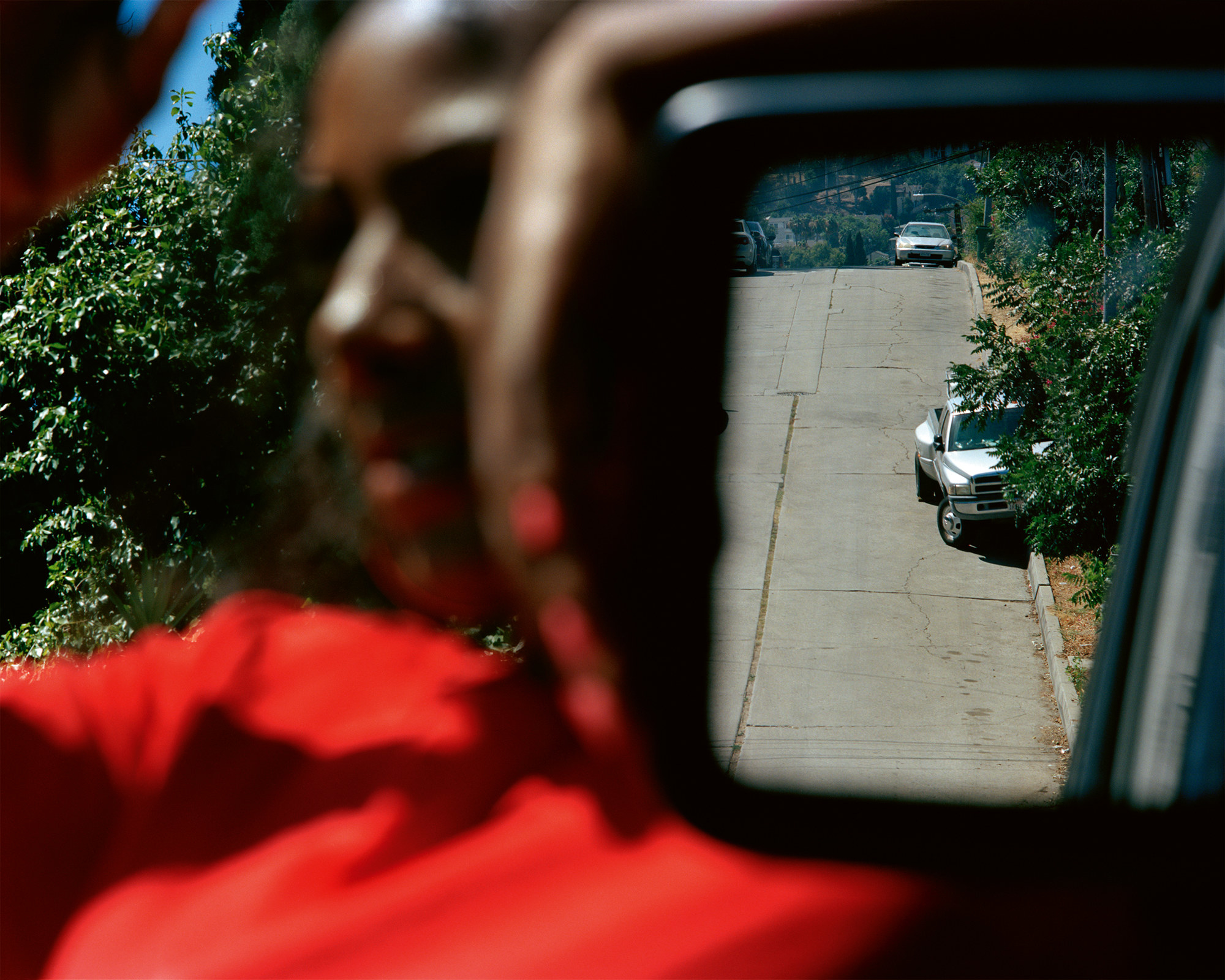 A photo where a woman is out of focus, but the road in the rearview mirror is in focus