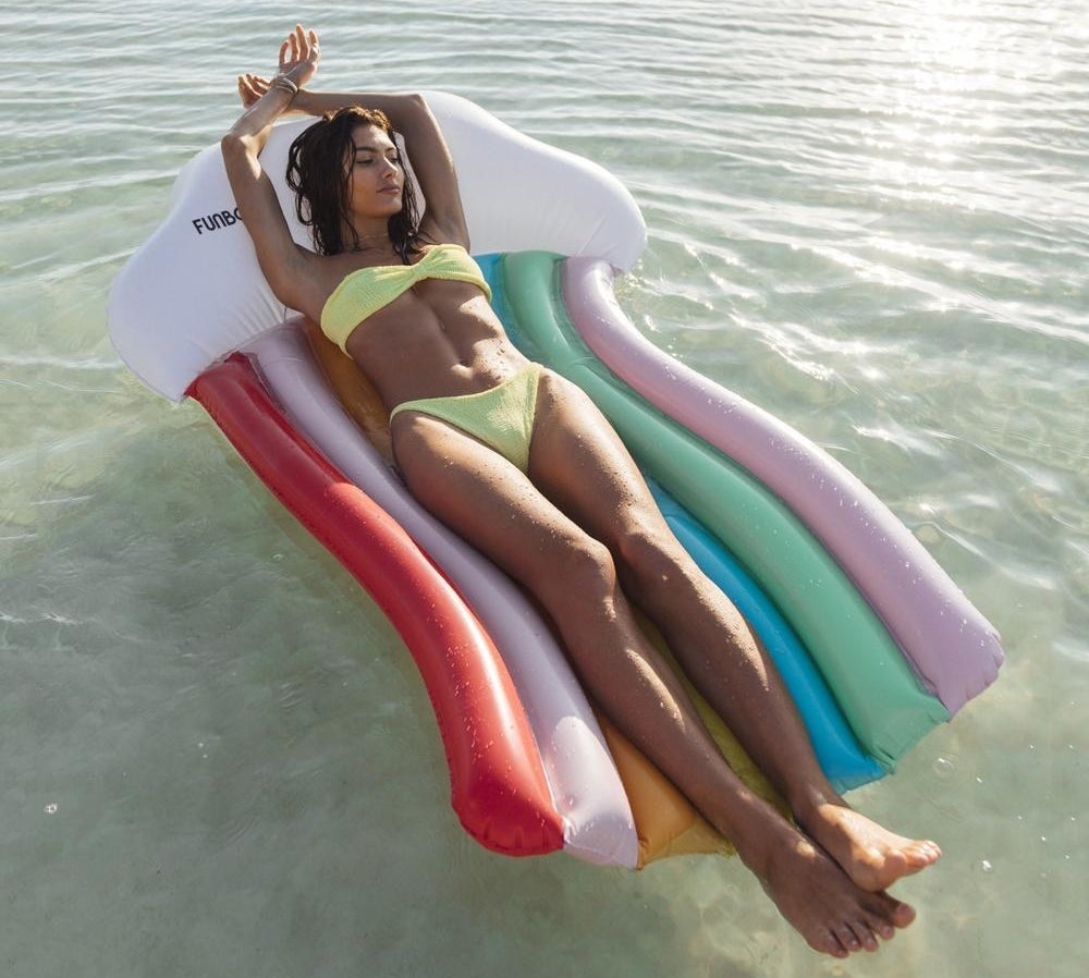 a model laying on a pool floatie shaped like a cloud with a rainbow