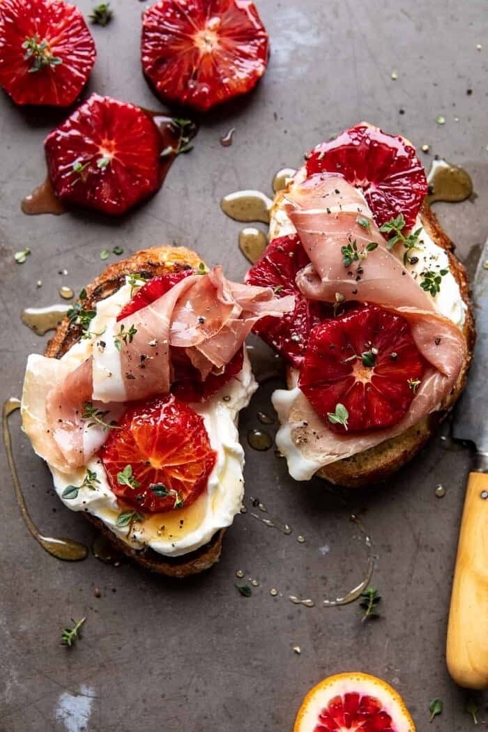 Two toasts topped with ricotta, prosciutto, and honey drizzle.