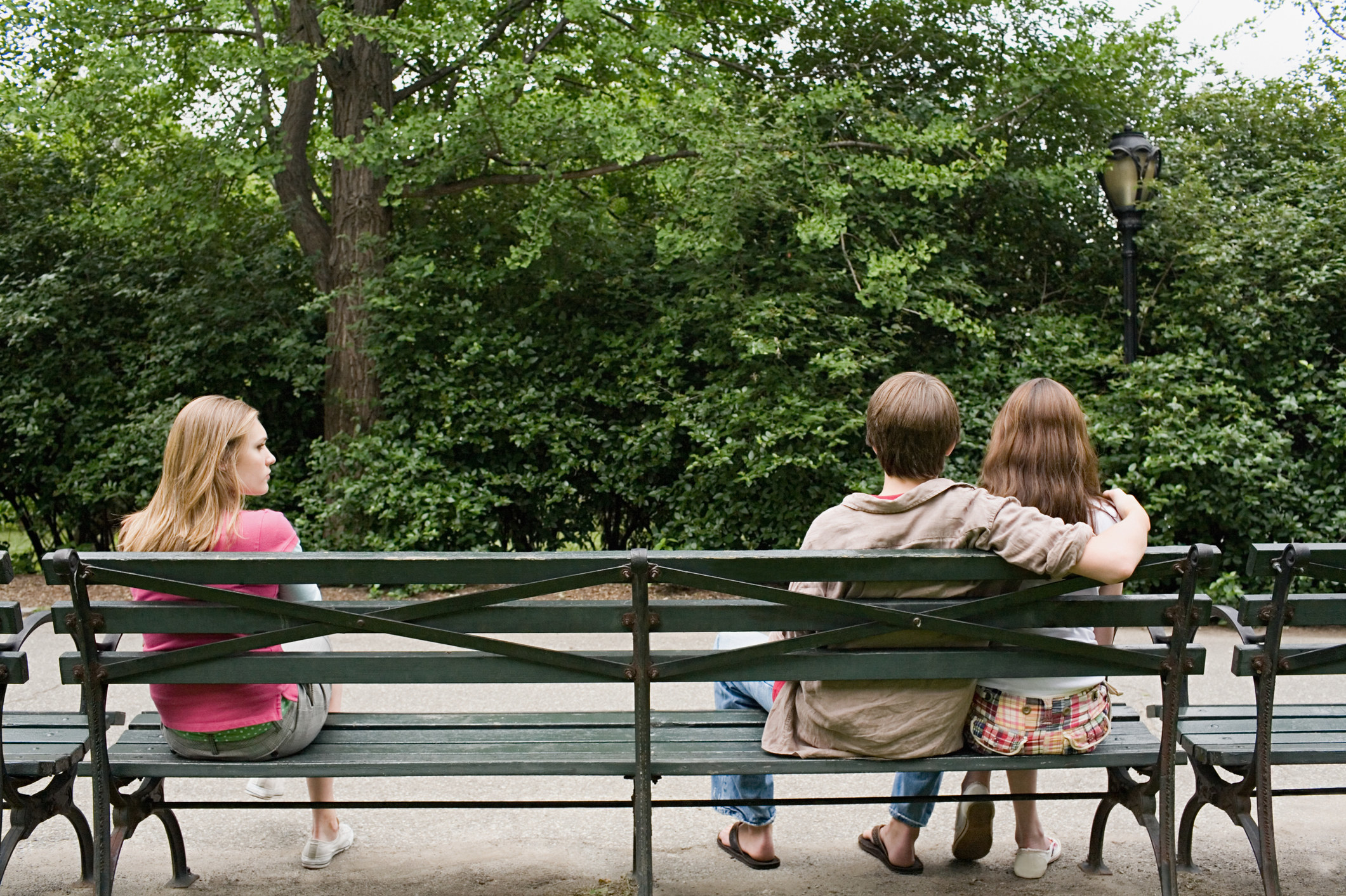 a woman alone at one end of a bench and a couple cuddling at the other
