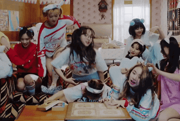 The nine members of Twice sit down in front of a tv