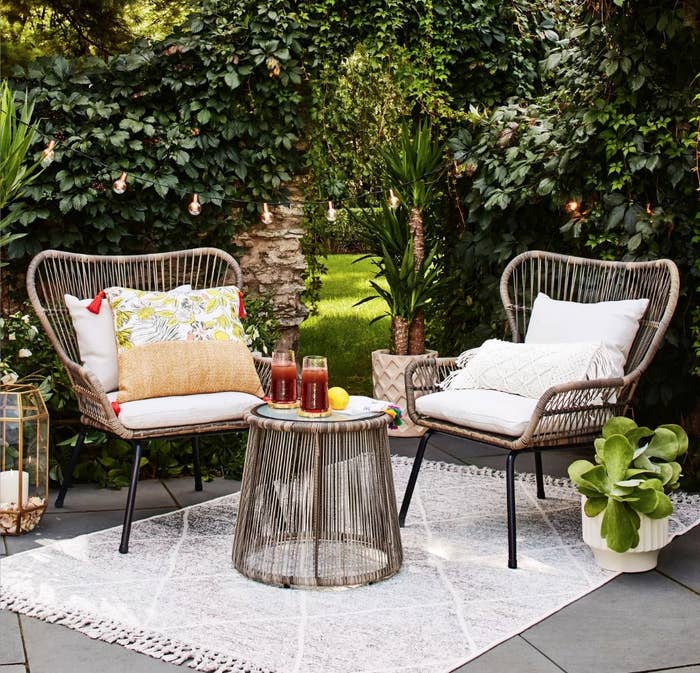 A 3-piece, brown rattan patio set with white cushions over an outdoor rug