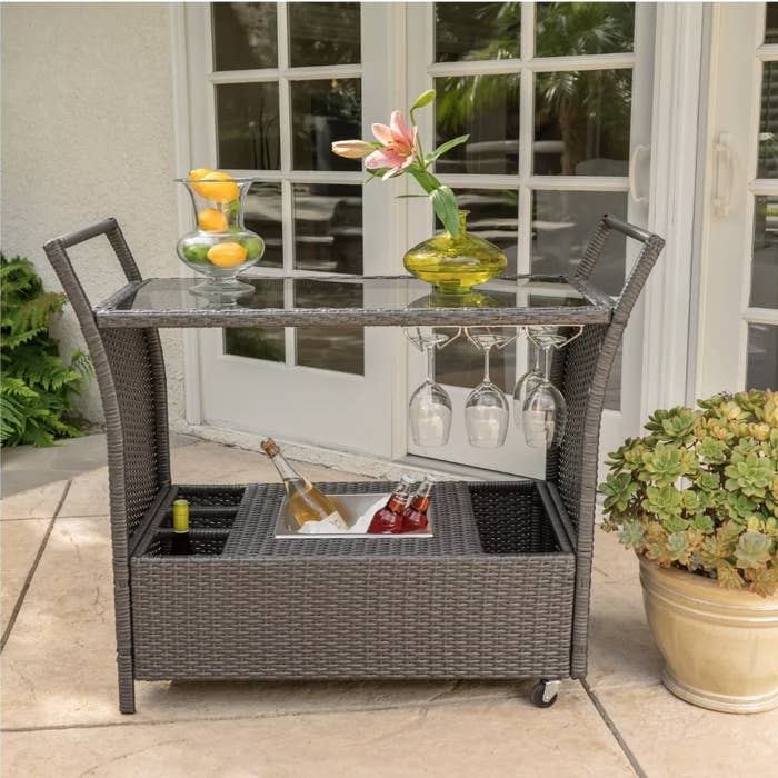 A gray wicker bar cart on wheels on a patio