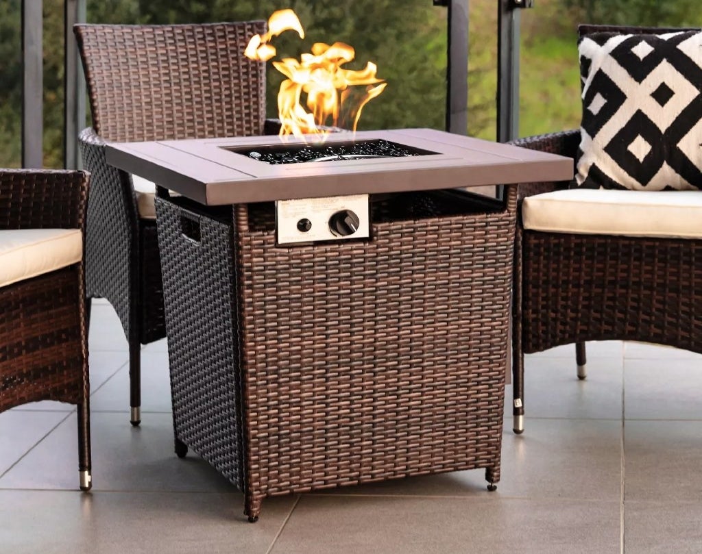 A brown, wicker, propane fire pit on a patio surrounded by wicker chairs