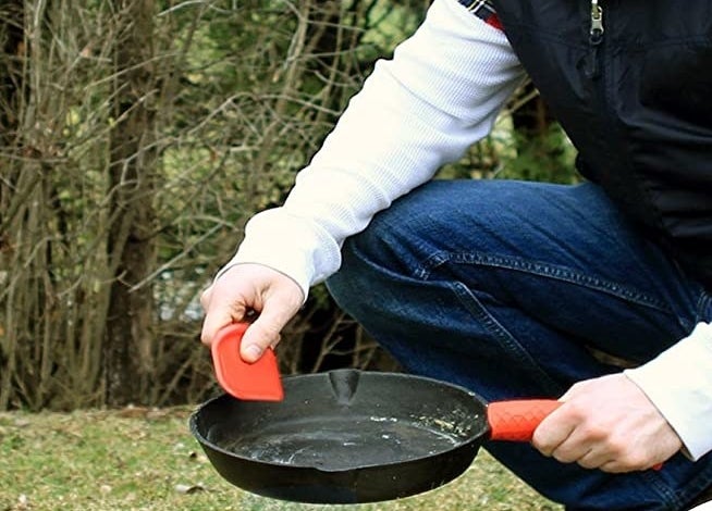 hand uses red square scraper on dirty cast iron skillet