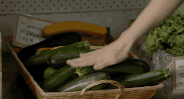 Woman feeling cucumber, tasting it and then putting it in her shopping basket