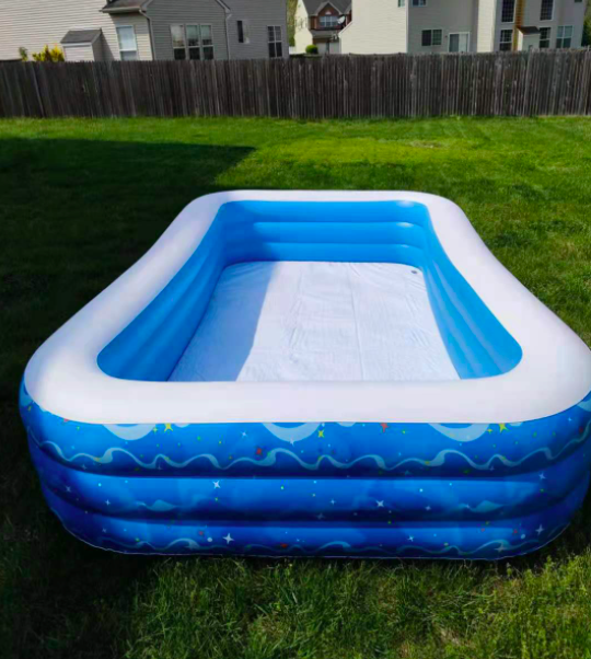the blow-up pool has a rectangle shape and is sitting in a grassy yard beside a lounging chair and small table with drinks on it
