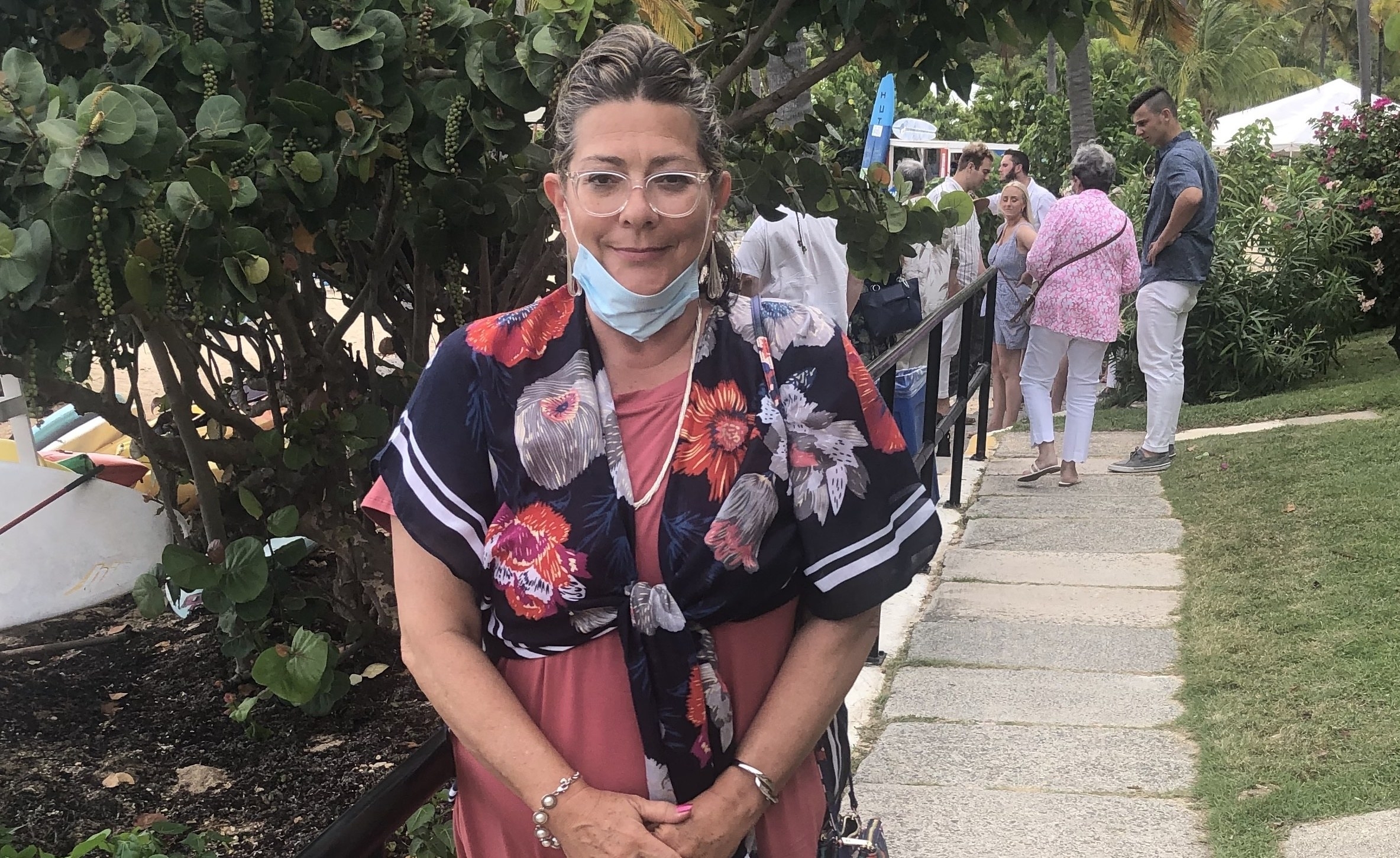 Lisa Ditalia, with a surgical face mask sitting under her chin, smiles at the camera while standing outdoors