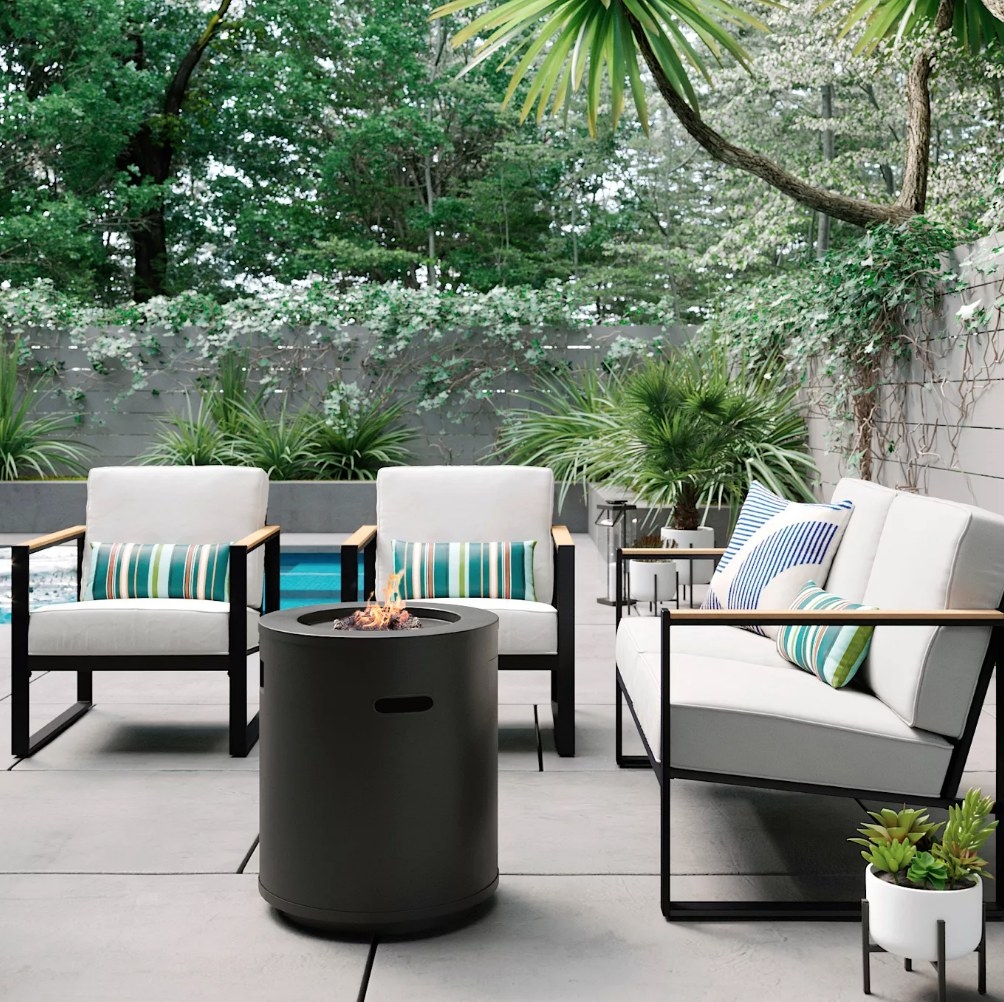 A black, round, metal fire column on a patio surrounded by lounge chairs