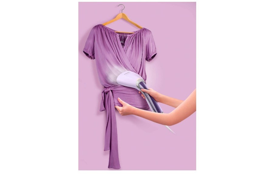 A person steam ironing a dress that&#x27;s hanging on a wall