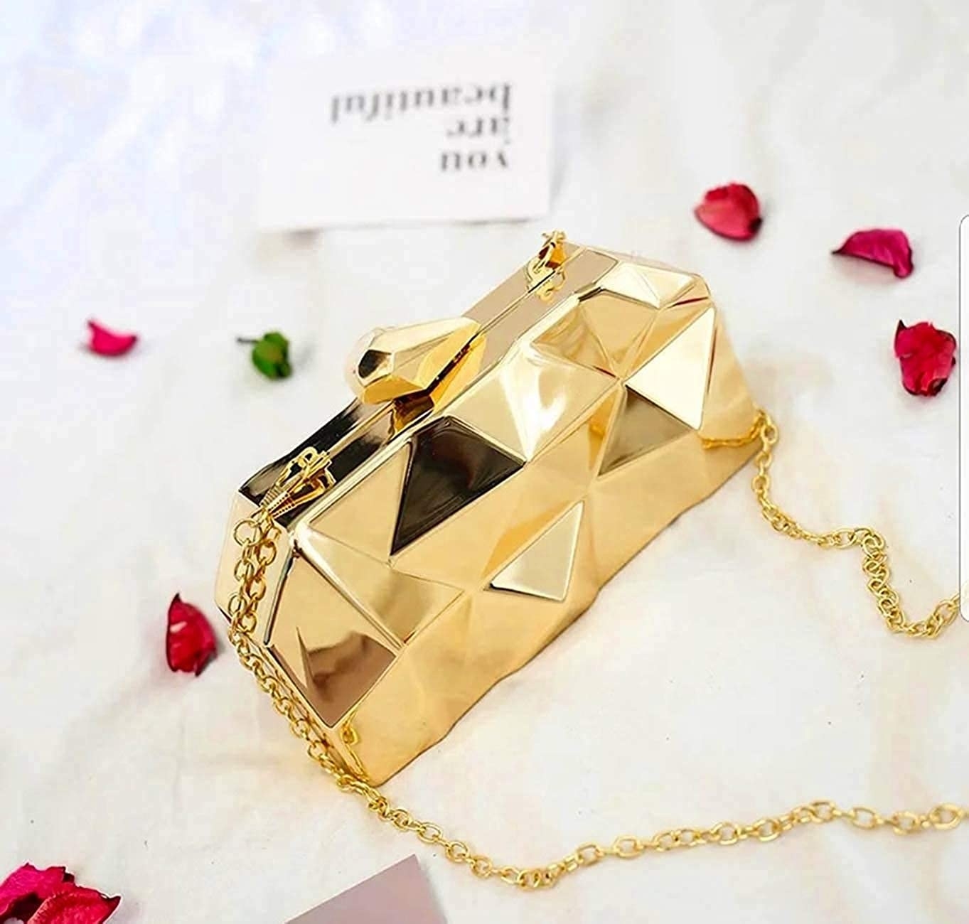 A golden clutch next to rose petals