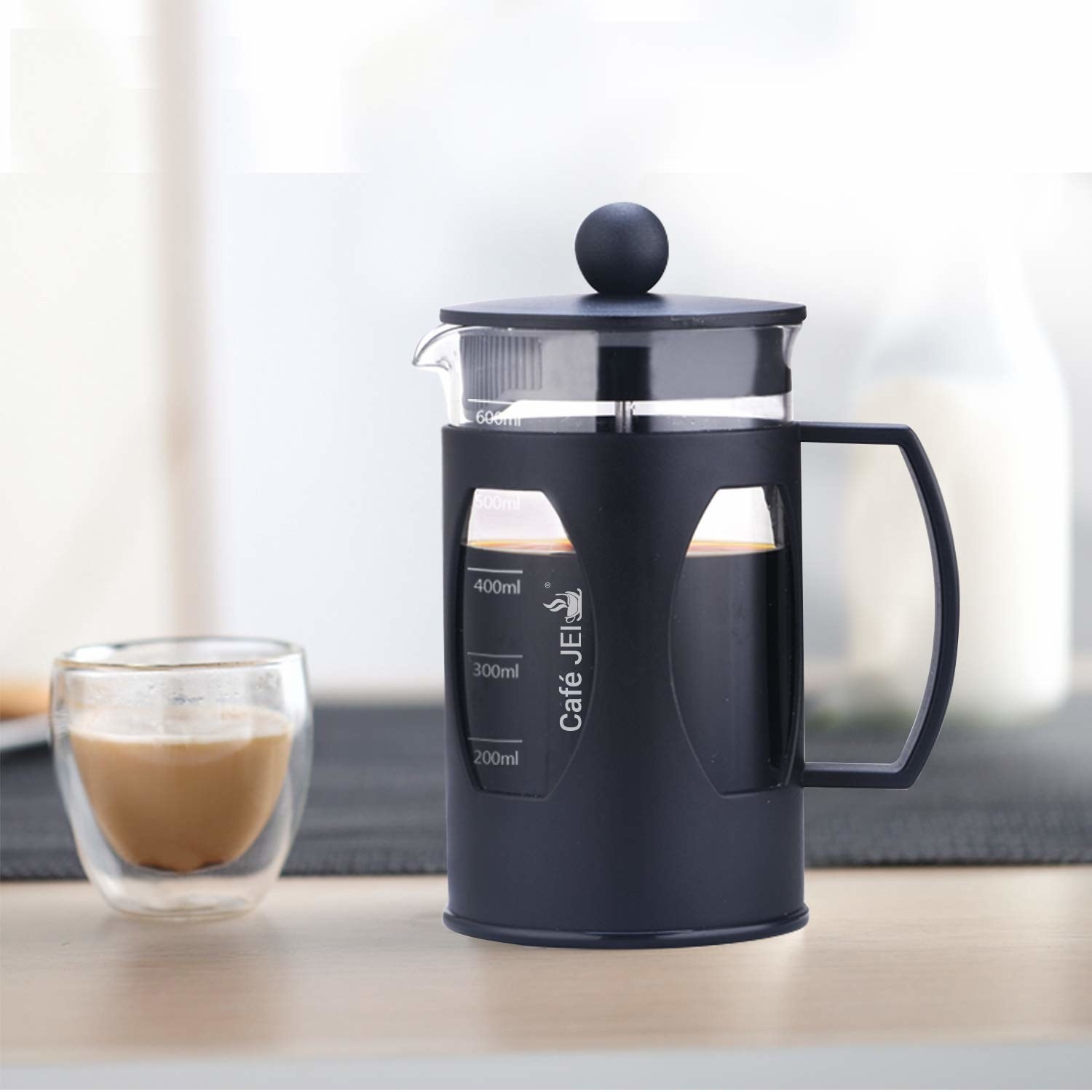 A French Press coffee maker next to a cup of coffee