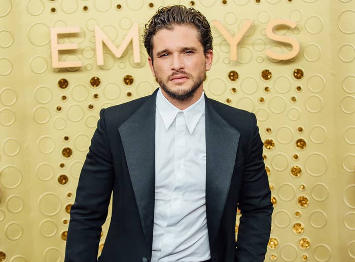 Kit looks serious while wearing a suit jacket and white button down at an event