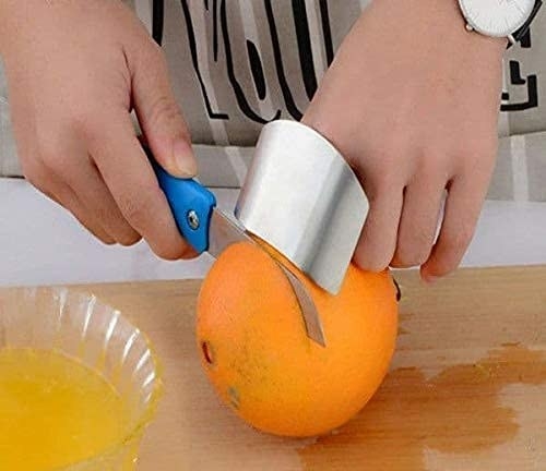 A person using the steel guard to shield their fingers while slicing an orange